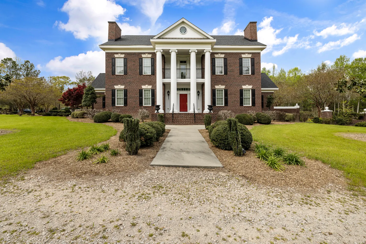 A red-brick colonial home with white columns and a manicured lawn under a clear blue sky